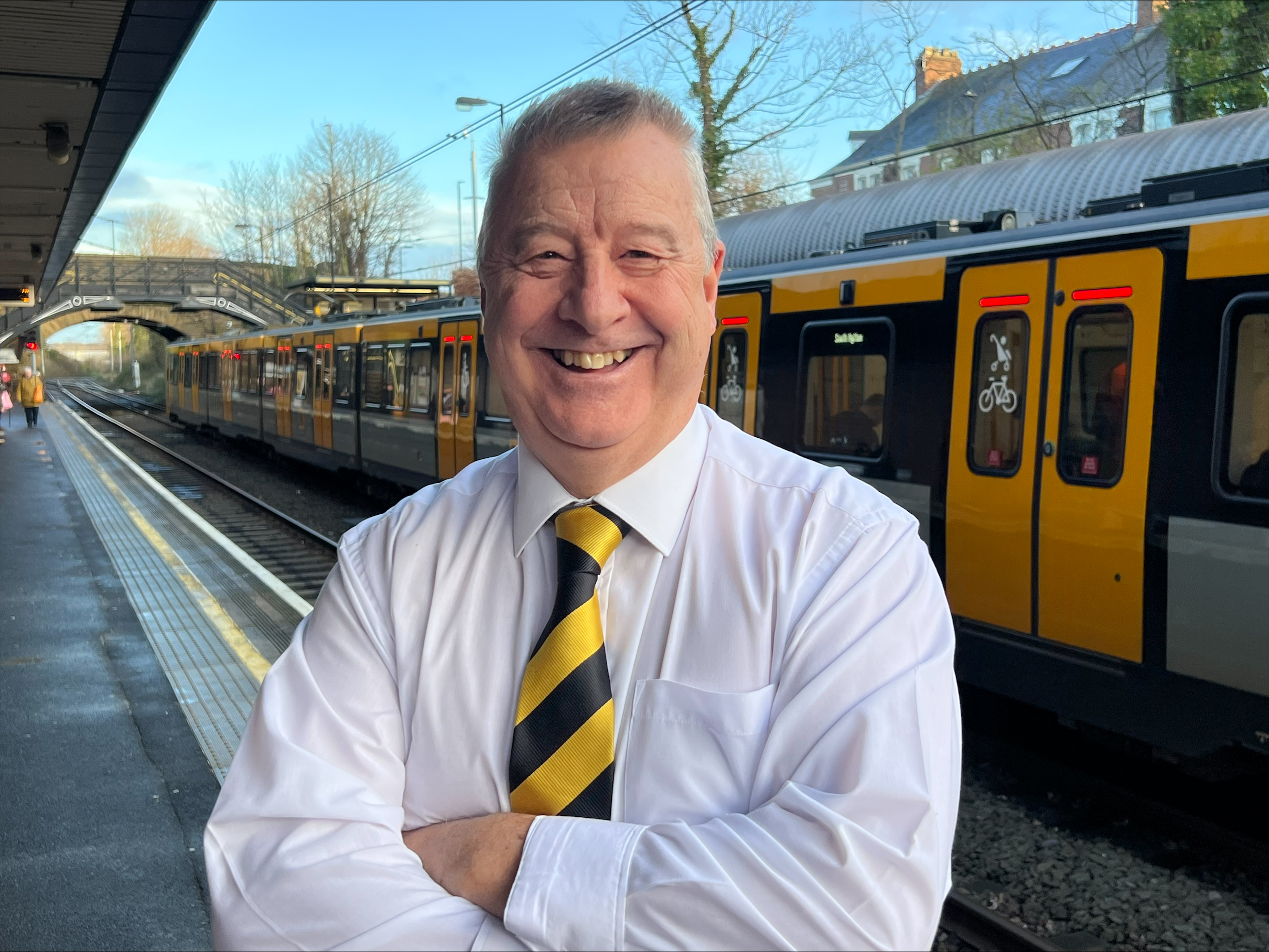 A man in a shirt and tie stands on a platform in front of a Metro train
