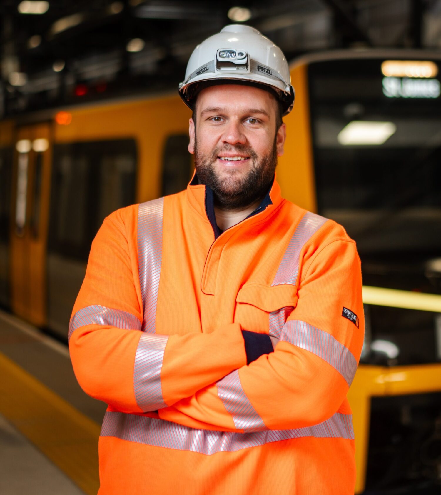 A man wearing a high vis orange jacket and a white hard hat standing infront of a Metro train