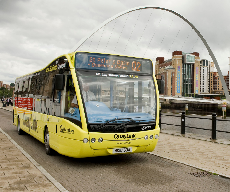 An image of a small yellow bus on Gateshead Quayside with the Millennium Bridge in the background