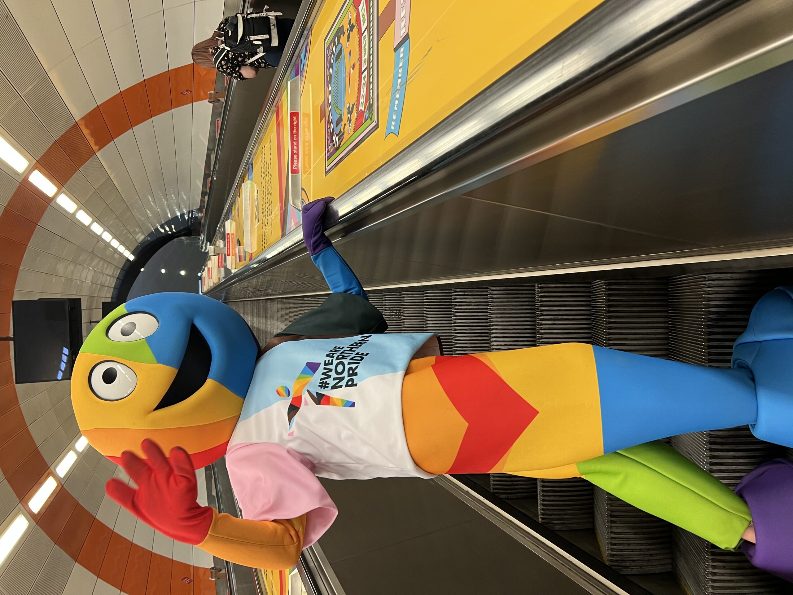 A brightly coloured Pride mascot on an escalator at Haymarket metro station