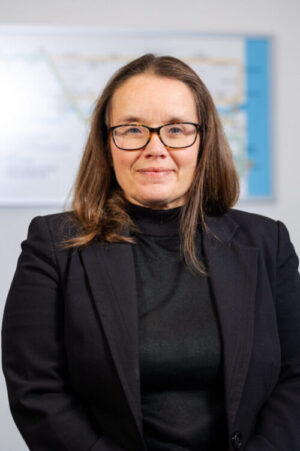 A woman in a black jacket and glasses looking at the camera