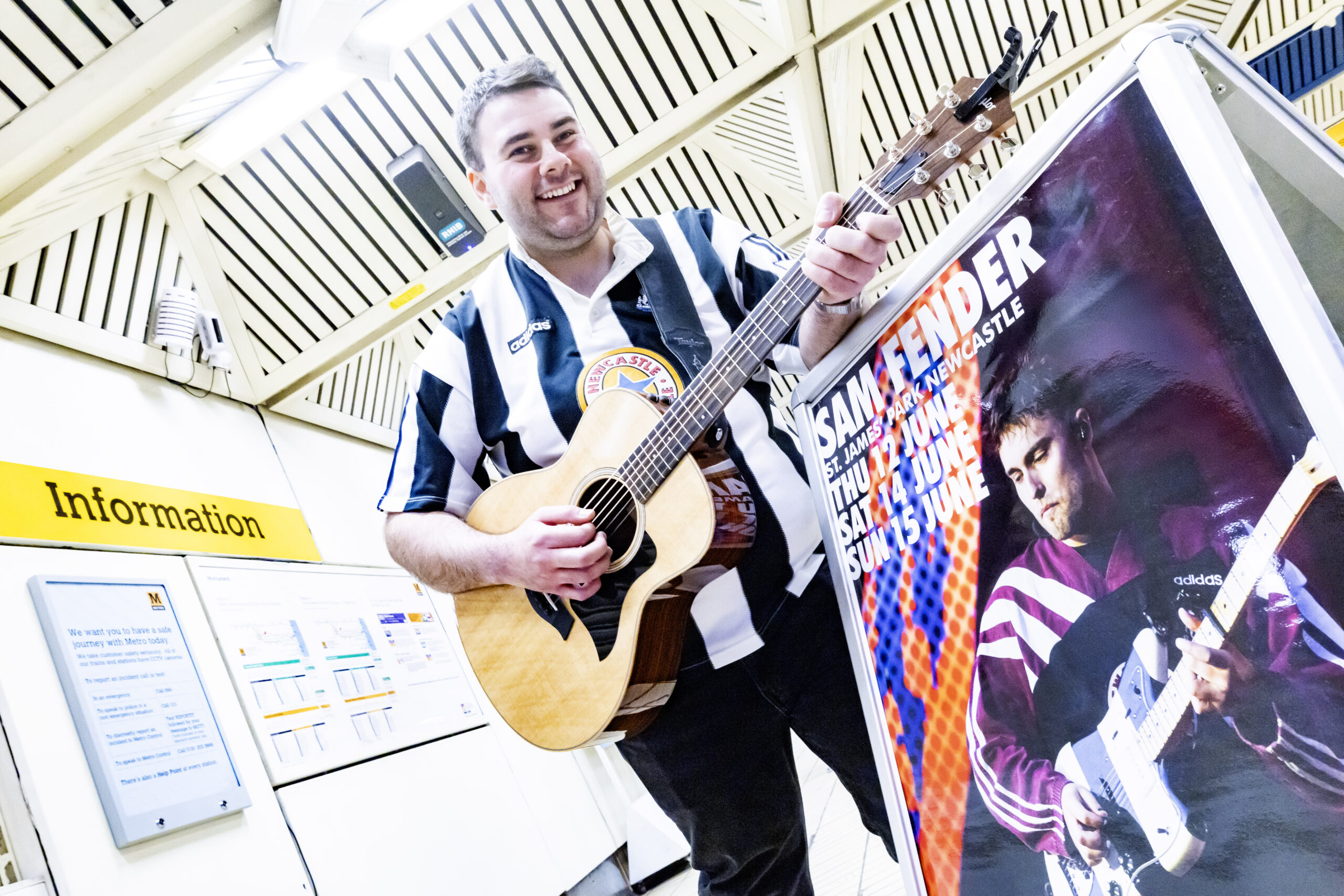 A man in a Newcastle football shirt playing a guitar in a Metro station