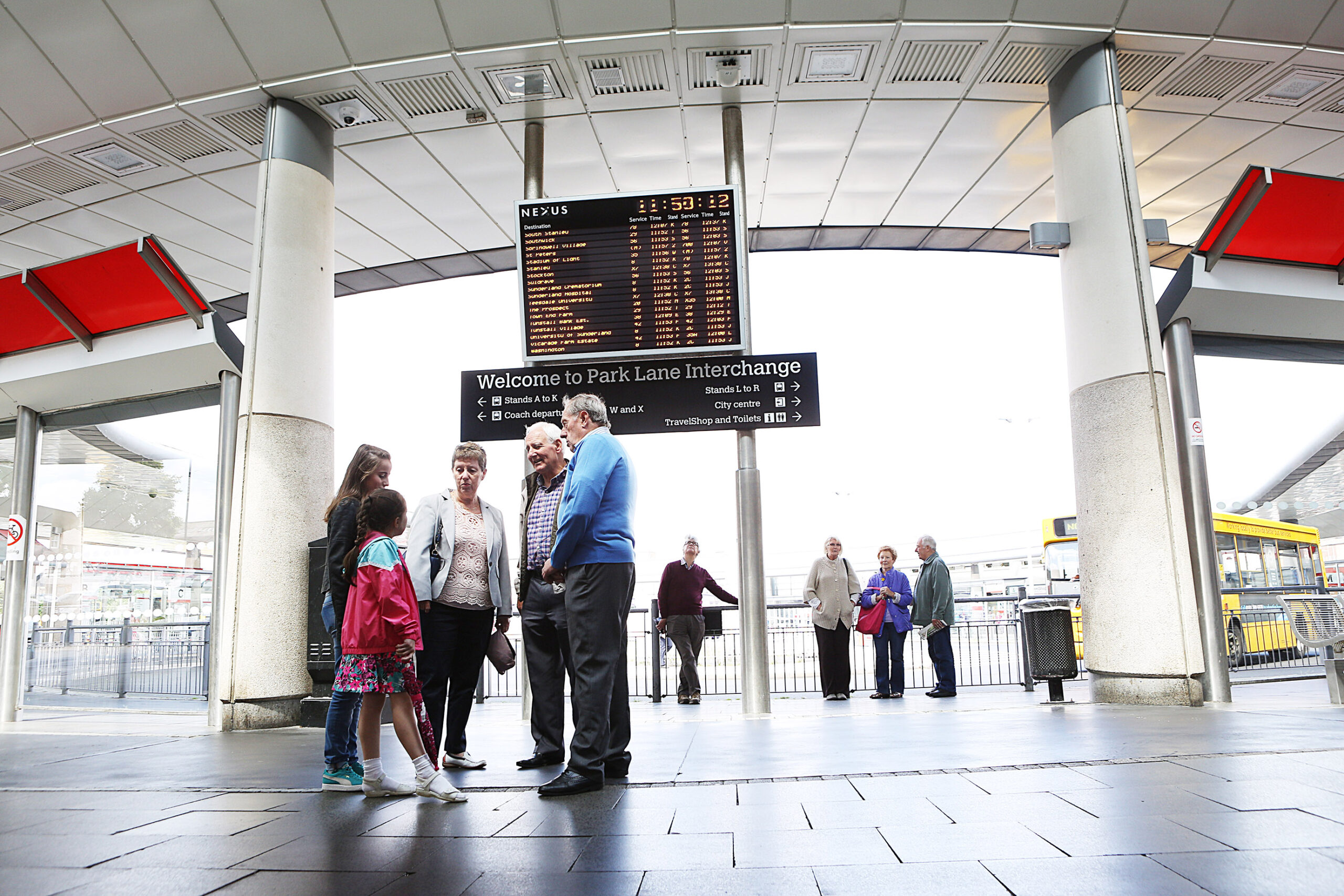 An image of Park Lane bus station with a family standing infront of the departure board